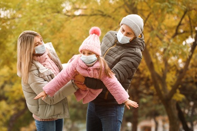 Photo of Family in medical masks playing outdoors on autumn day. Protective measures during coronavirus quarantine