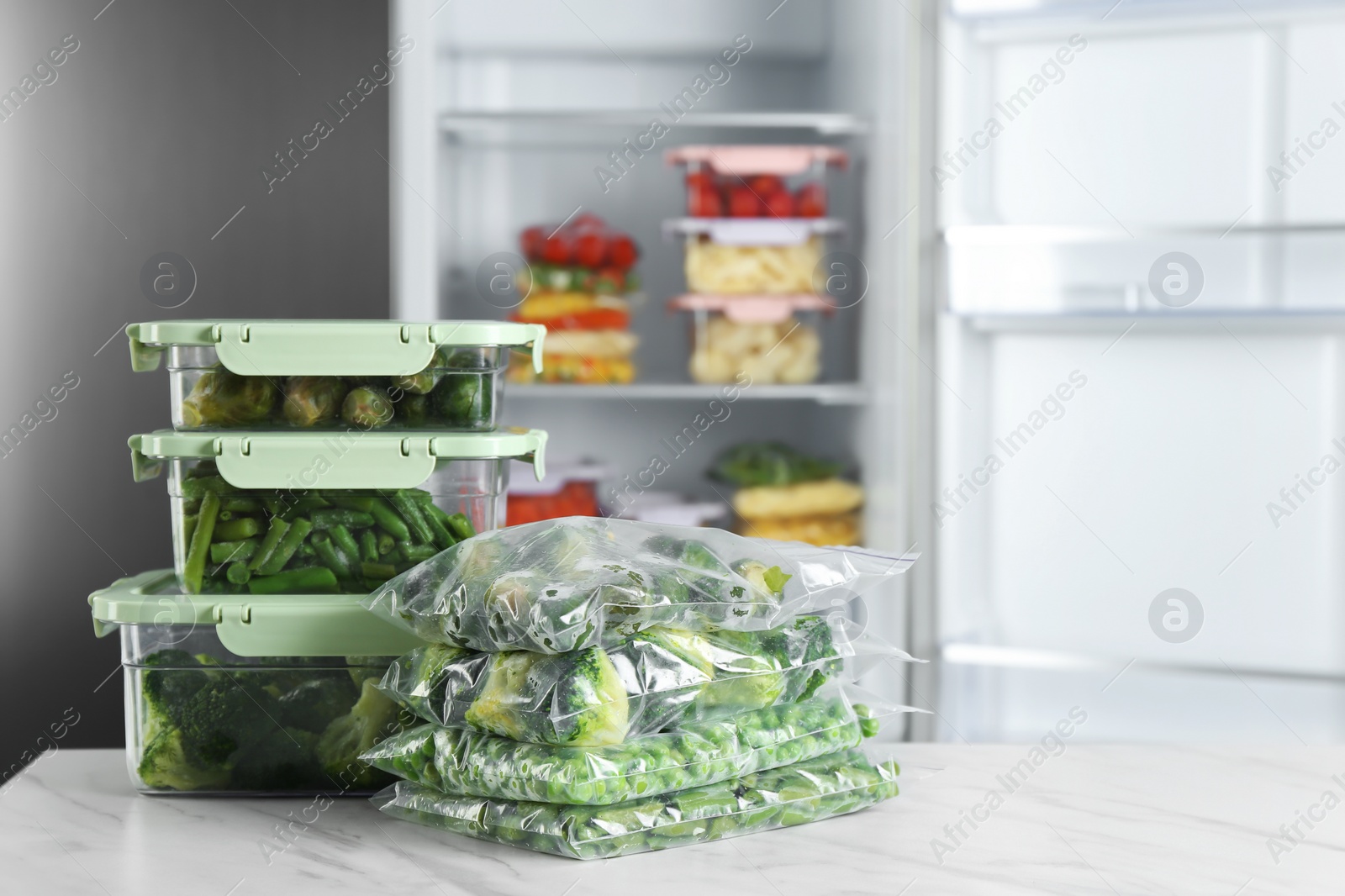 Photo of Different frozen vegetables on white marble table near open refrigerator