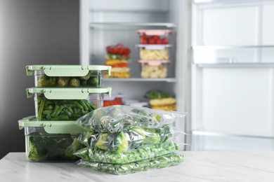 Different frozen vegetables on white marble table near open refrigerator