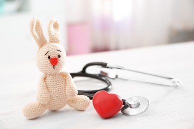 Photo of Toy bunny, stethoscope and heart on table indoors, space for text. Children's doctor