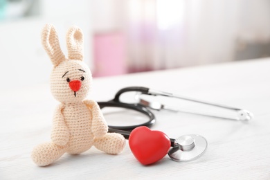 Toy bunny, stethoscope and heart on table indoors, space for text. Children's doctor