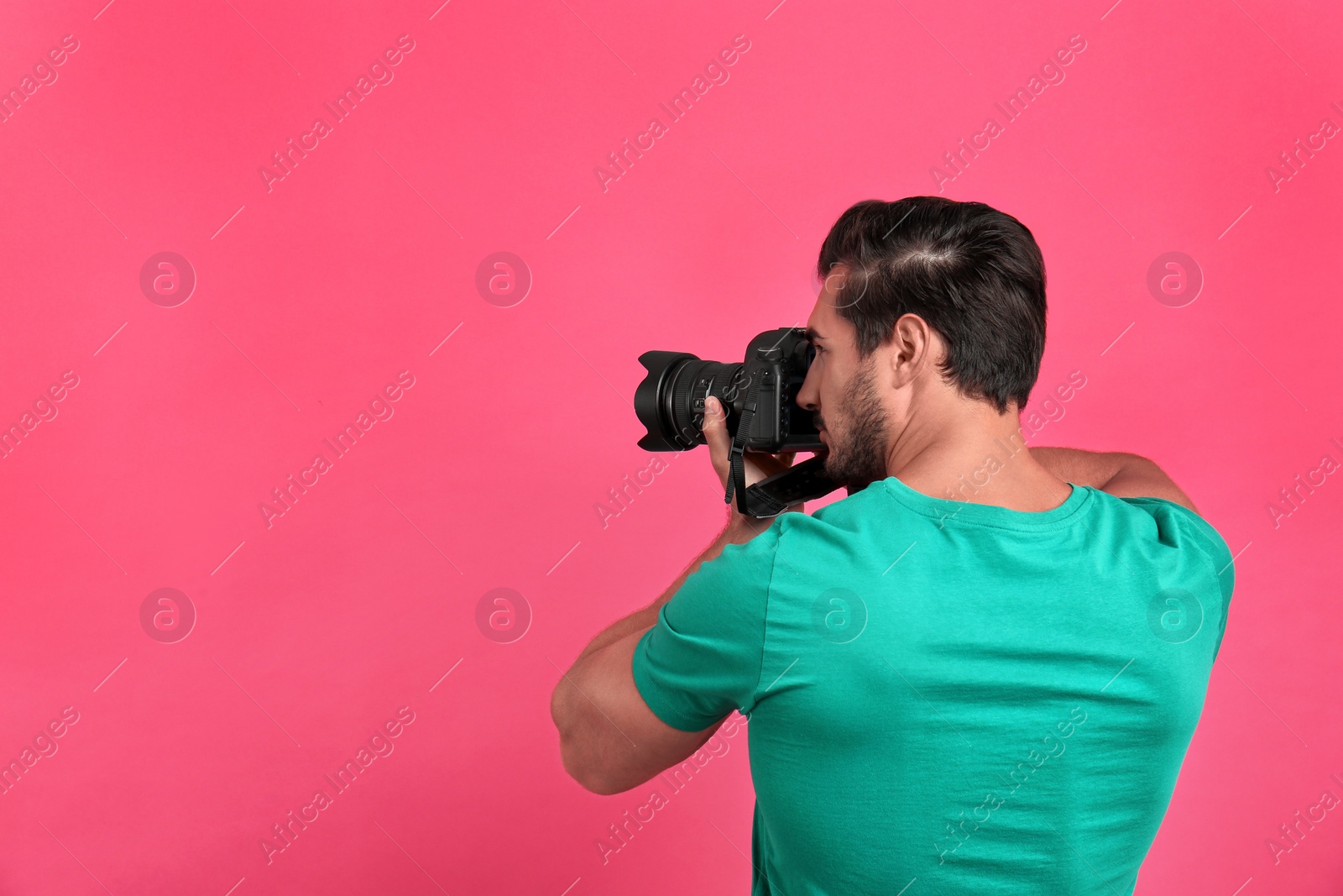 Photo of Young professional photographer taking picture on pink background. Space for text