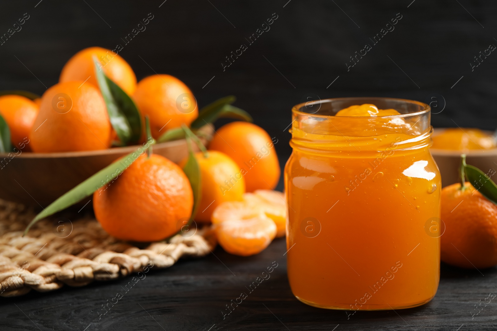 Photo of Tasty tangerine jam in glass jar on dark wooden table. Space for text