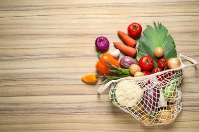 Photo of Fresh vegetables in eco mesh bag on wooden table, flat lay. Space for text
