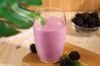 Photo of Delicious blackberry smoothie in glass and berries on wooden table, closeup