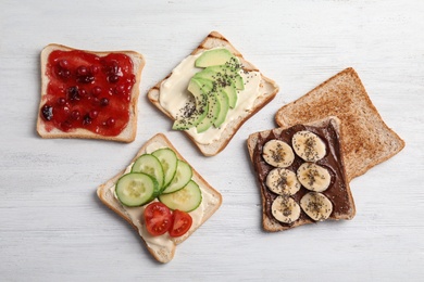 Photo of Slices of bread with different toppings on white wooden table, flat lay