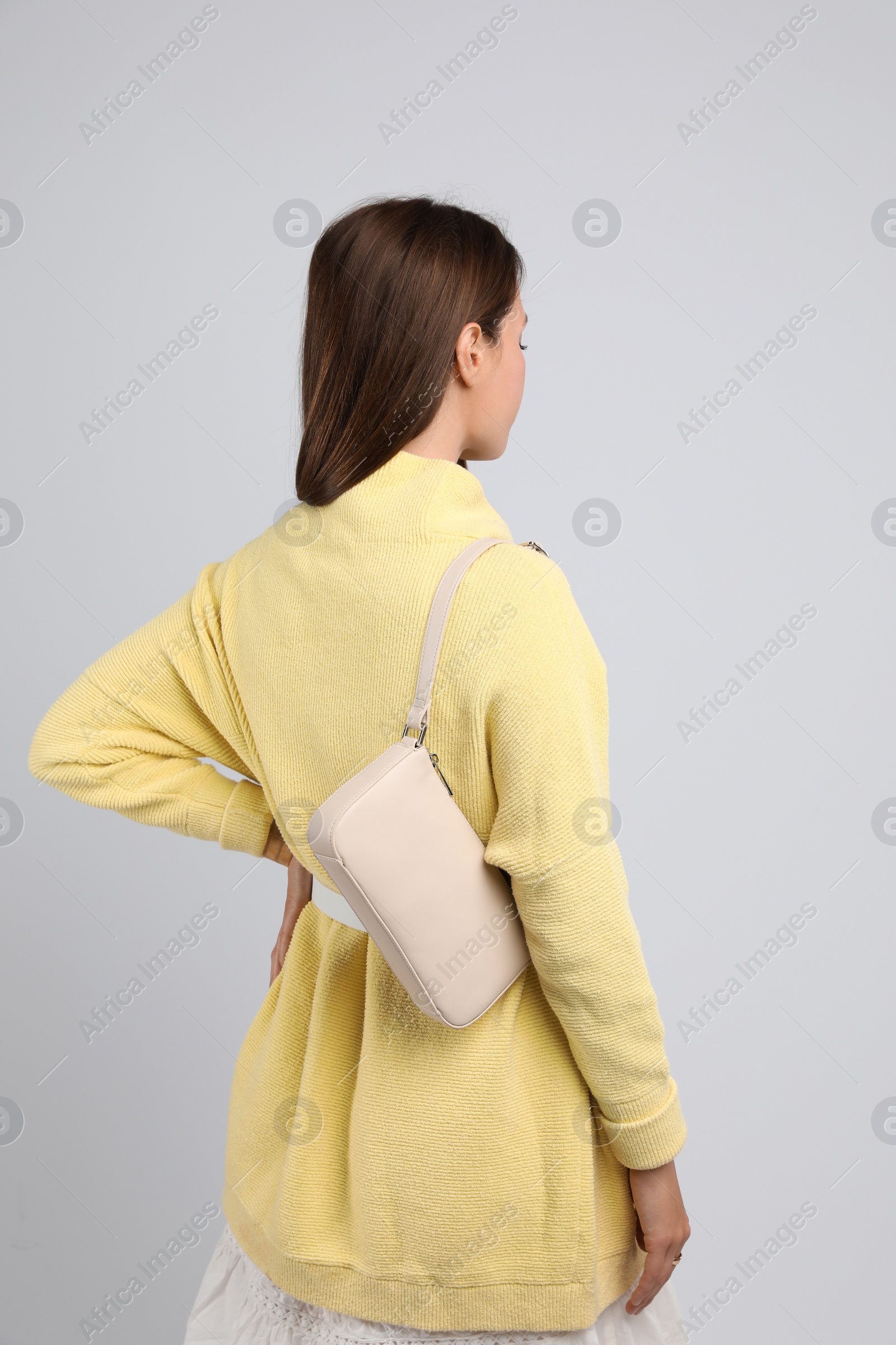 Photo of Fashionable young woman with stylish bag on light background, back view