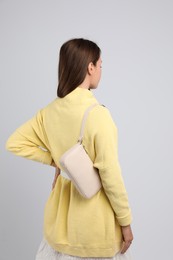 Fashionable young woman with stylish bag on light background, back view