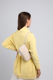 Photo of Fashionable young woman with stylish bag on light background, back view