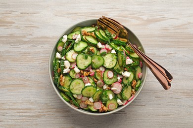 Photo of Bowl of delicious cucumber salad, spoon and fork on white wooden table, top view