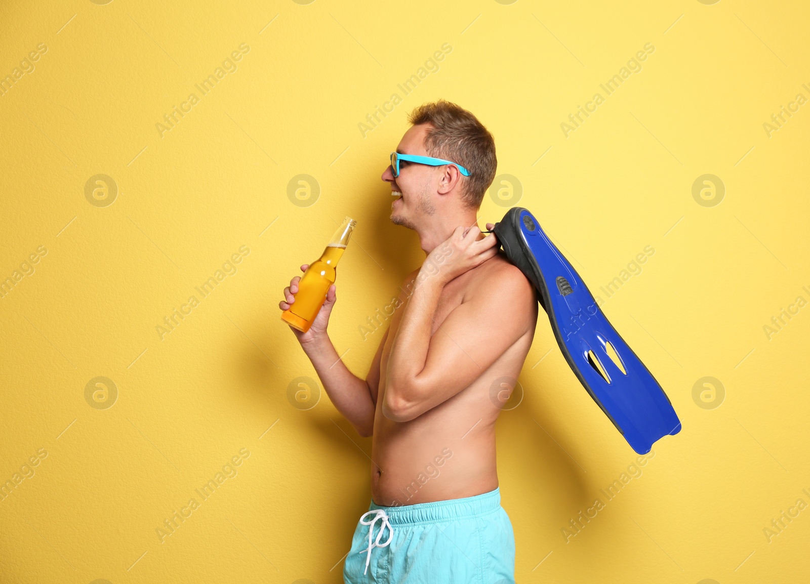 Photo of Shirtless man with bottle of drink and flippers on color background