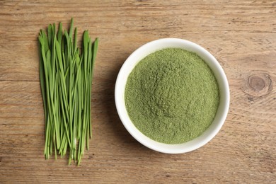 Photo of Wheat grass powder in bowl and fresh green sprouts on wooden table, flat lay