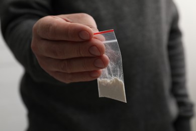 Drug addiction. Man with plastic bag of cocaine on light background, closeup