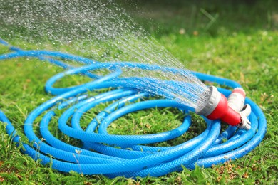 Photo of Water spraying from hose on green grass outdoors