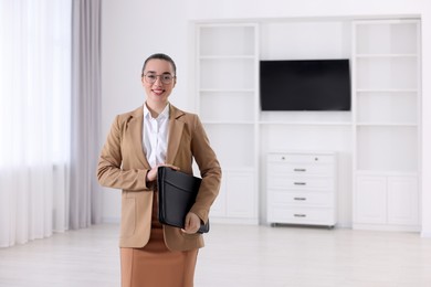 Photo of Happy real estate agent with leather portfolio indoors. Space for text