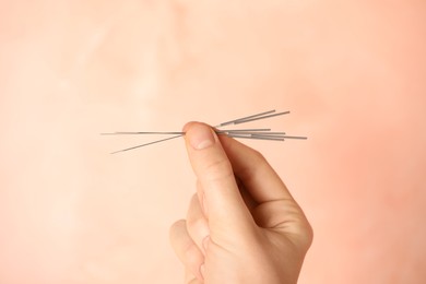 Photo of Woman holding needles for acupuncture on pink background, closeup