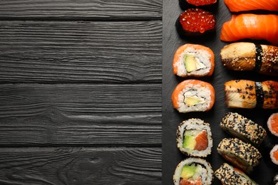 Photo of Set of delicious sushi rolls on black wooden table, top view. Space for text