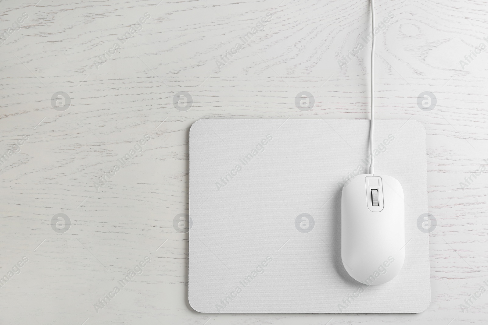 Photo of Modern wired optical mouse and pad on white wooden table, top view. Space for text