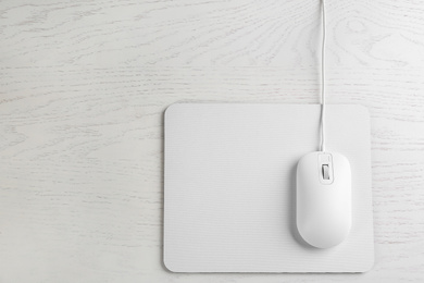 Photo of Modern wired optical mouse and pad on white wooden table, top view. Space for text