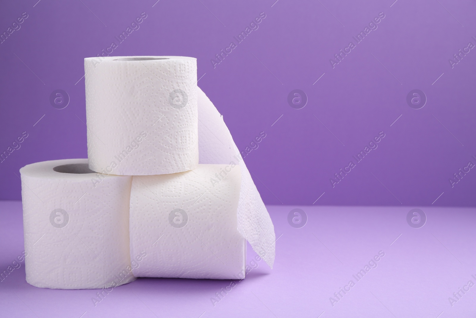 Photo of Soft toilet paper rolls on violet background, closeup. Space for text