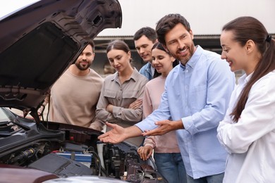 Photo of Driving school. Teacher explaining car engine to group outdoors