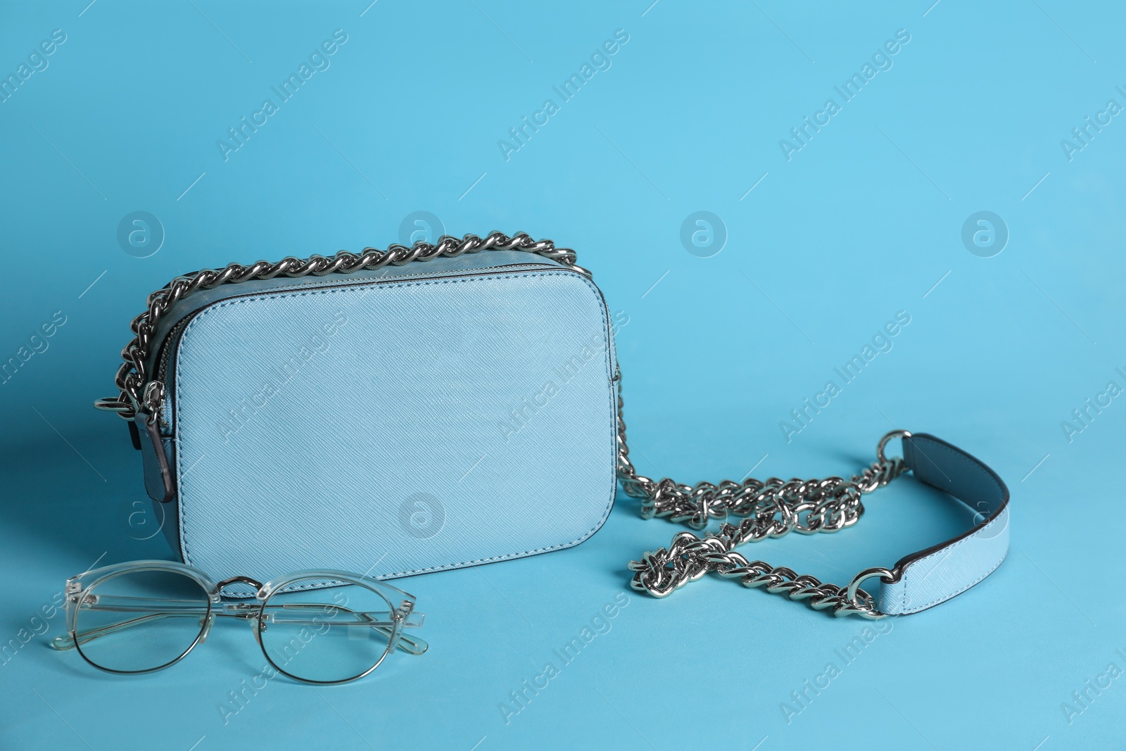 Photo of Stylish woman's bag and glasses on light blue background