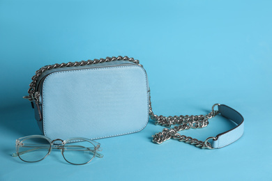 Stylish woman's bag and glasses on light blue background