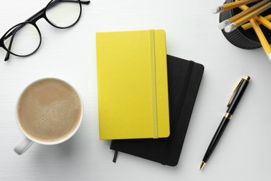 Photo of Different notebooks, cup of coffee, glasses and stationery on white wooden table, flat lay