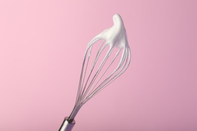 Photo of Whisk with whipped egg whites on pink background