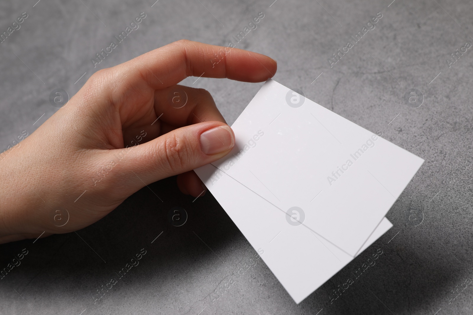 Photo of Woman holding blank cards at grey table, closeup. Mockup for design