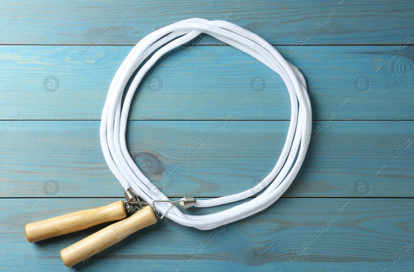 Photo of Skipping rope on light blue wooden table, top view. Sports equipment
