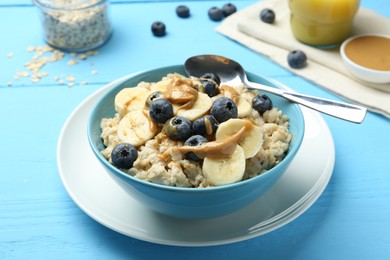 Tasty oatmeal with banana, blueberries and peanut butter served in bowl on light blue wooden table