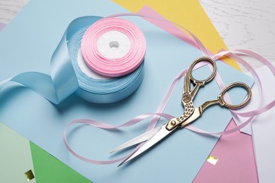 Beautiful scissors, satin ribbons and colorful paper sheets on white wooden table, above view