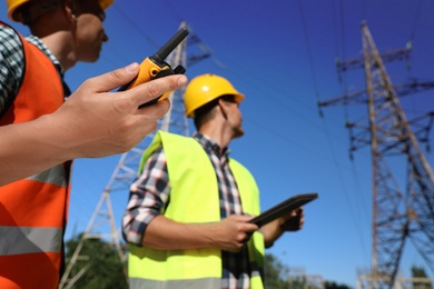 Professional electricians near high voltage towers, focus on hand with portable radio station