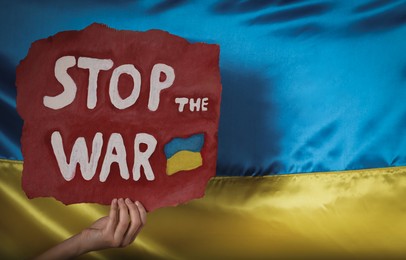 Photo of Woman holding poster with words Stop the War near Ukrainian flag, closeup. Space for text