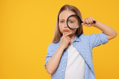 Cute little girl looking through magnifier on yellow background, space for text