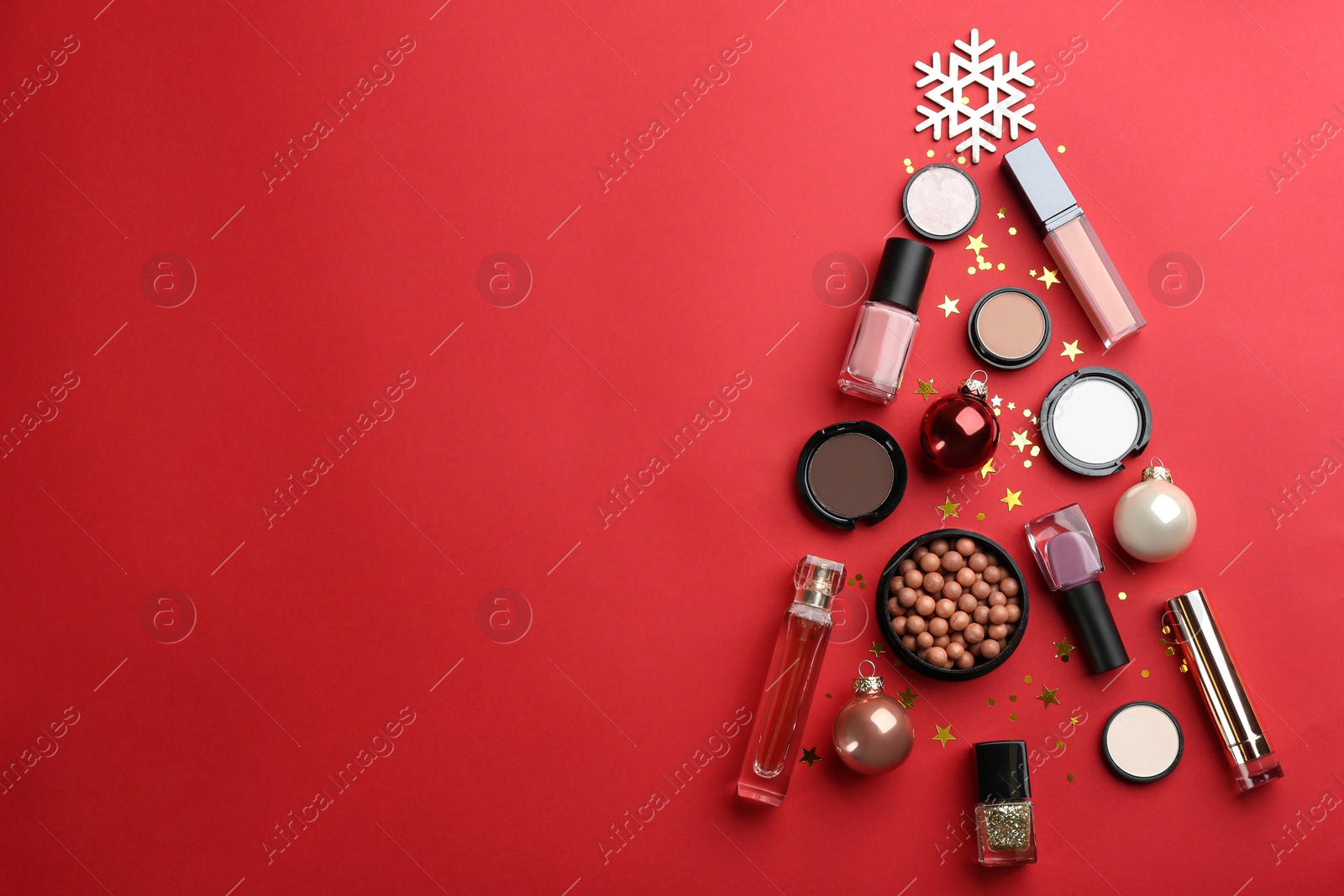 Photo of Christmas tree shape of decorative cosmetic products on red background, flat lay with space for text. Winter care