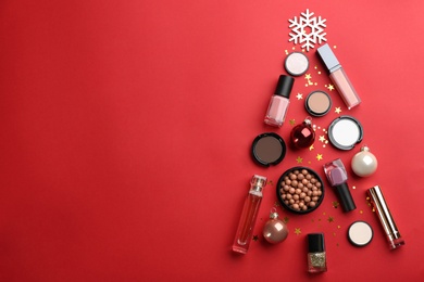 Photo of Christmas tree shape of decorative cosmetic products on red background, flat lay with space for text. Winter care