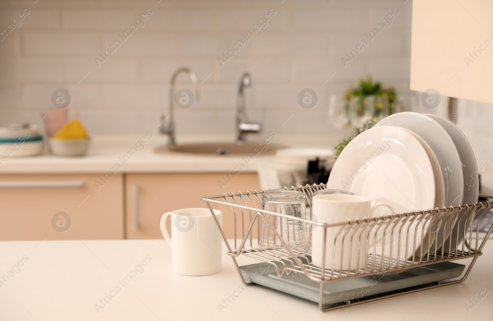 Photo of Dish drainer with clean dinnerware on table in kitchen. Space for text