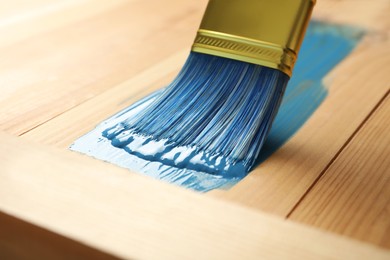 Photo of Applying blue paint onto wooden surface, closeup