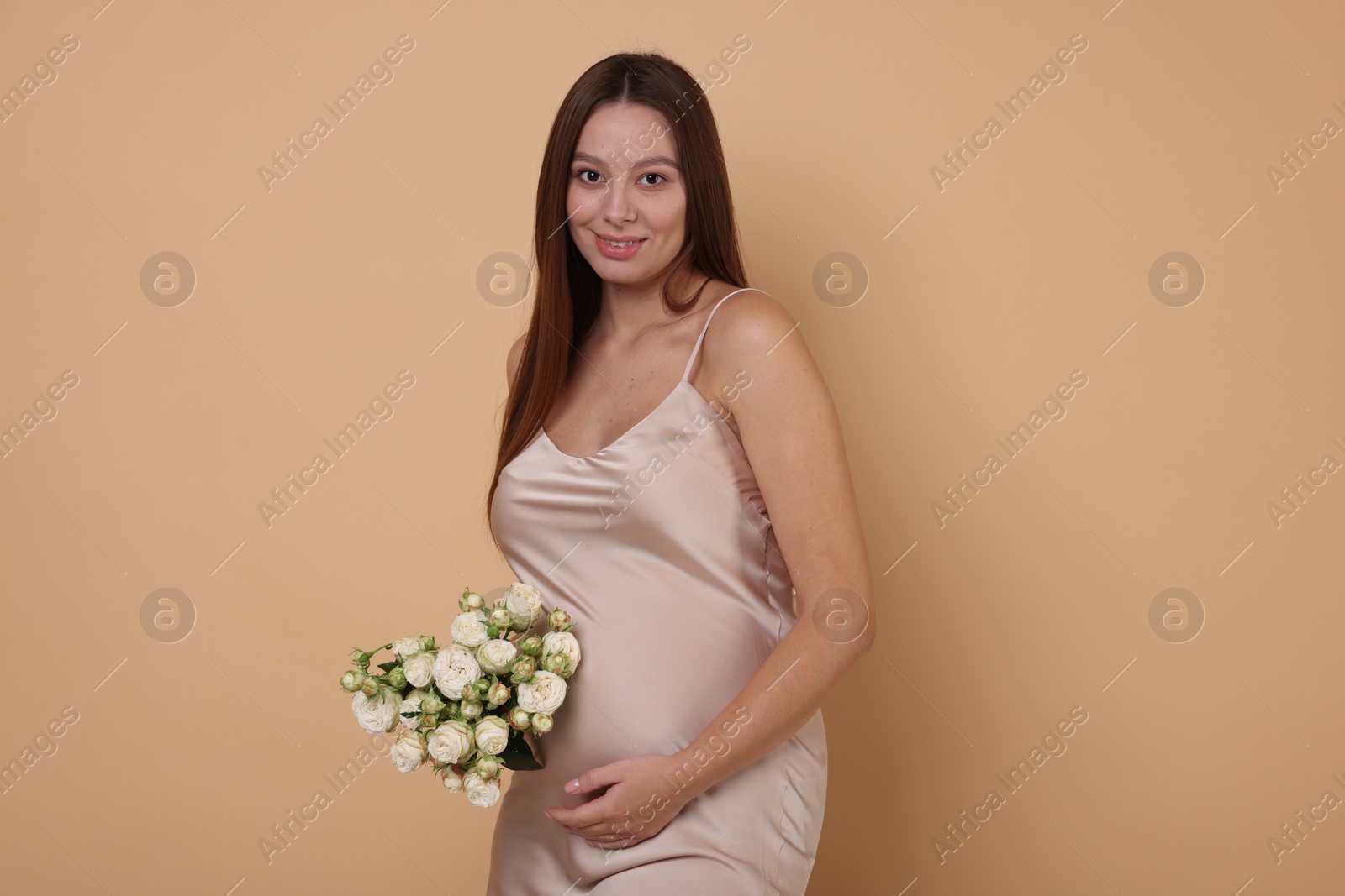 Photo of Beautiful pregnant woman in dress with bouquet of roses on beige background