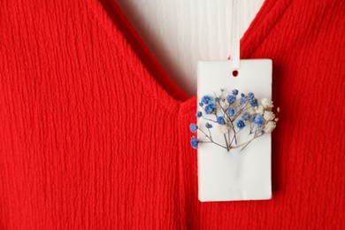 Photo of Scented sachet with flowers hanging near clothes, closeup view