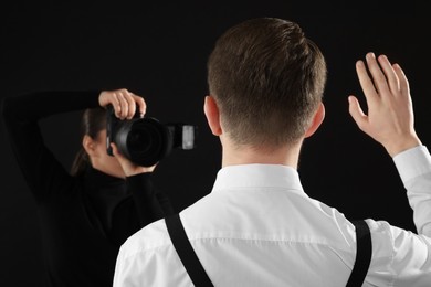 Photo of Professional photographer taking picture of man on black background, selective focus