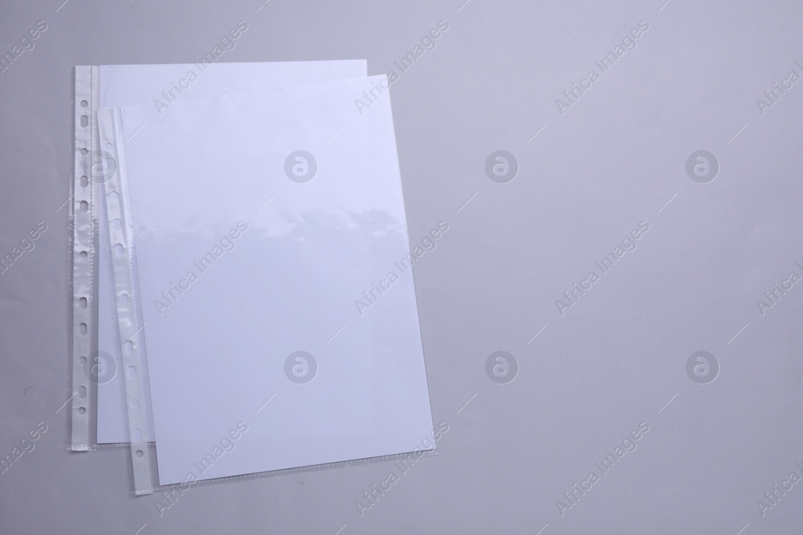 Photo of Punched pockets with paper sheets on light grey background, flat lay. Space for text