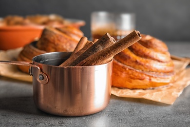 Photo of Saucepan with cinnamon sticks and rolls on table, closeup