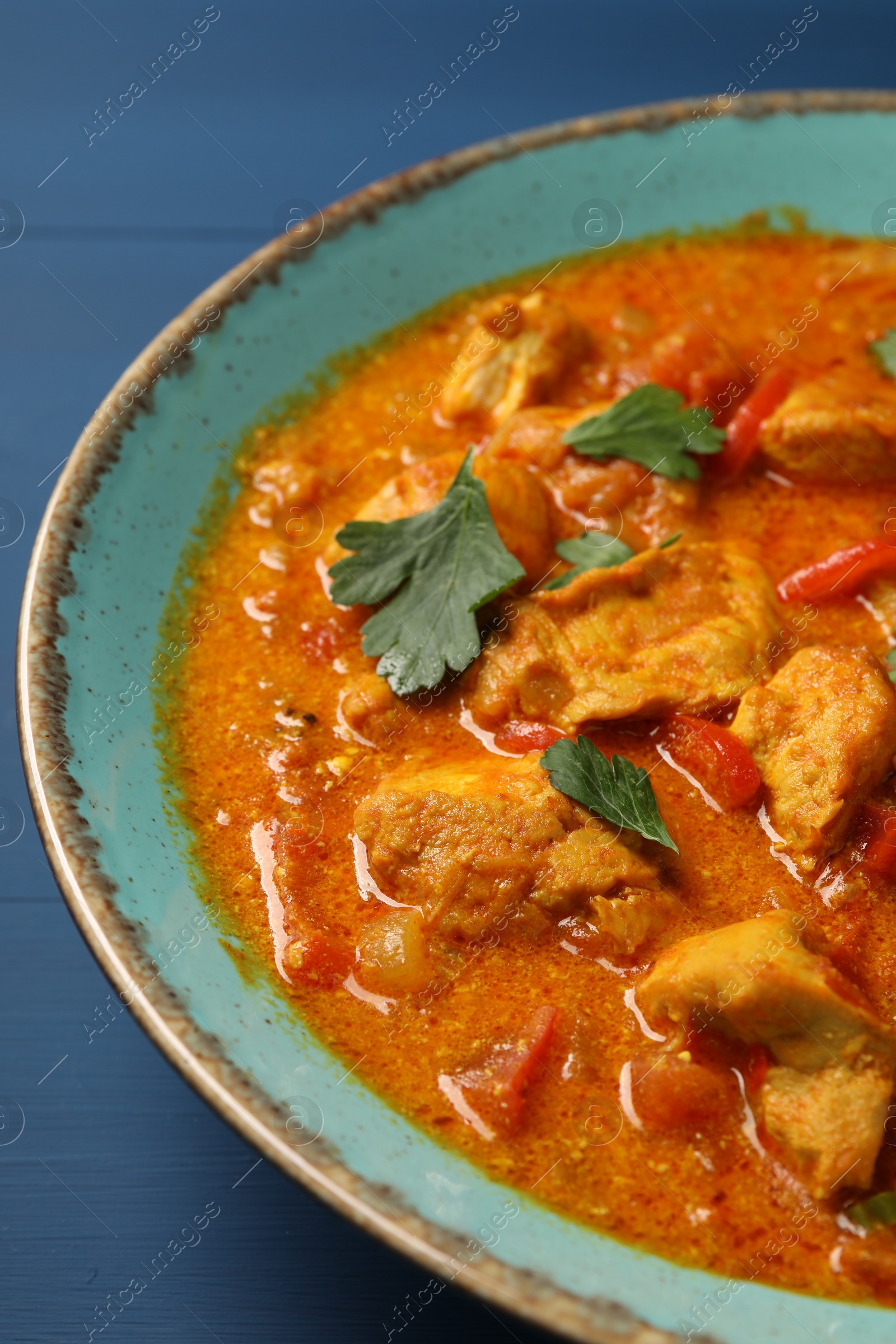 Photo of Delicious chicken curry on blue wooden table, closeup