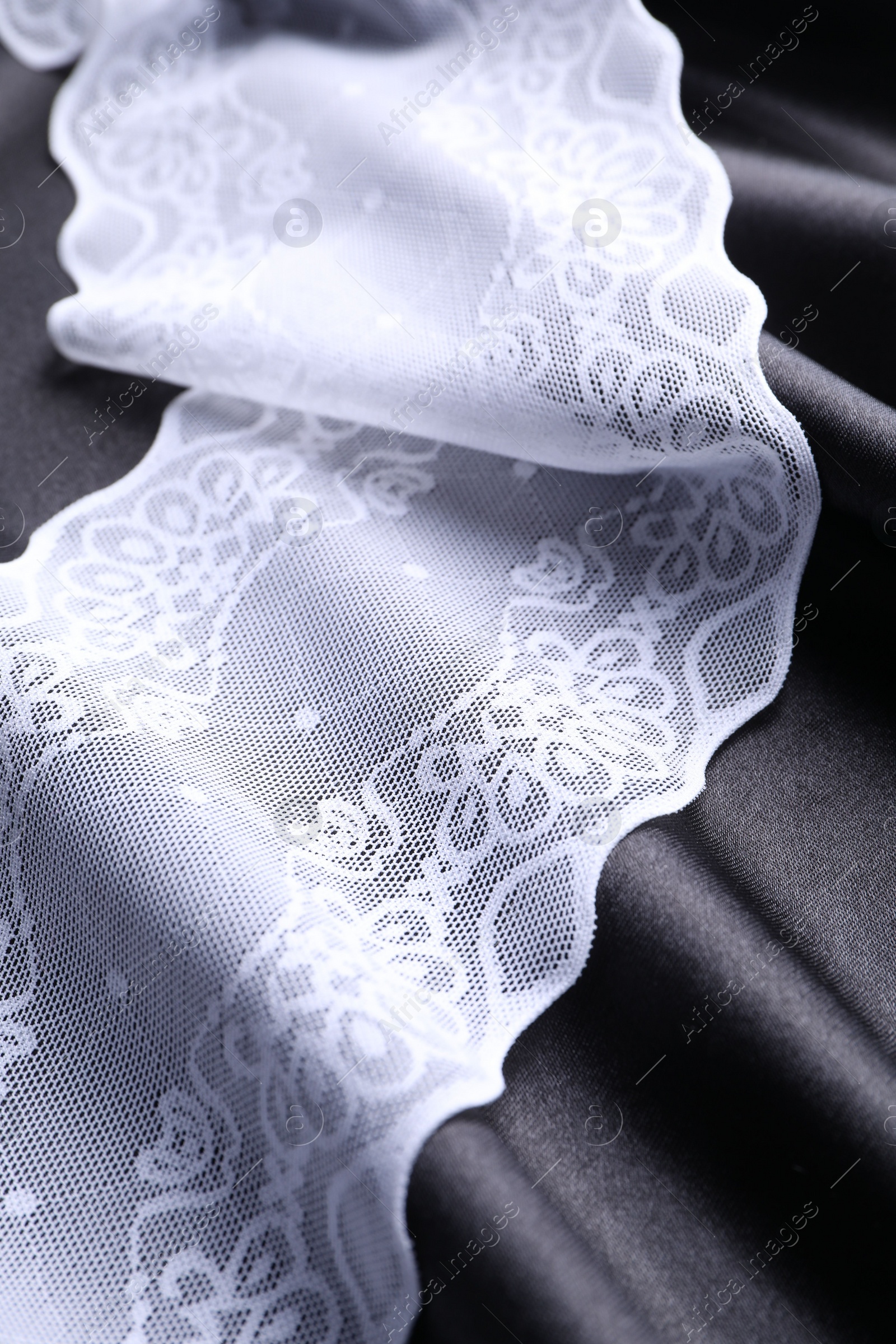 Photo of Beautiful white lace on black fabric, closeup