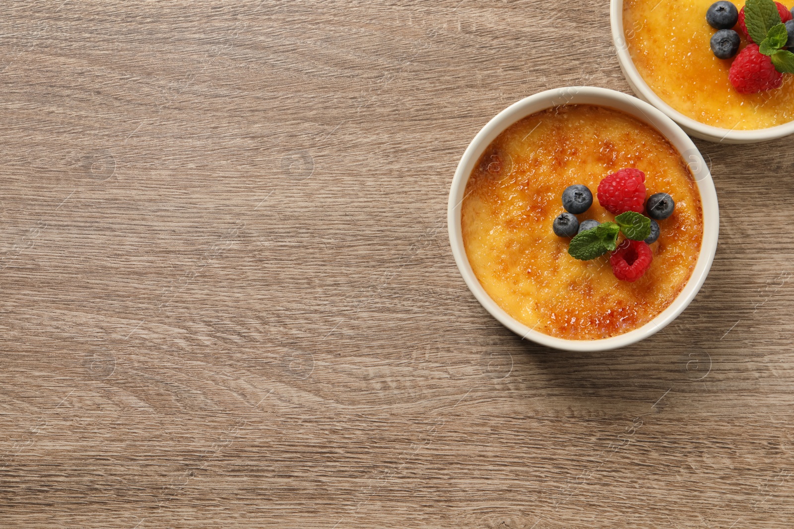 Photo of Delicious creme brulee with fresh berries on wooden table, flat lay. Space for text