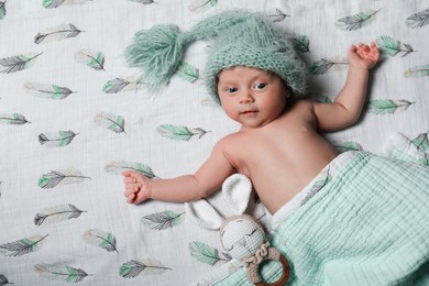 Photo of Cute newborn baby in warm hat with toy on bed, top view. Space for text