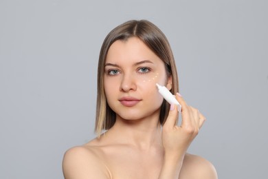 Photo of Young woman applying cream under eyes on light grey background
